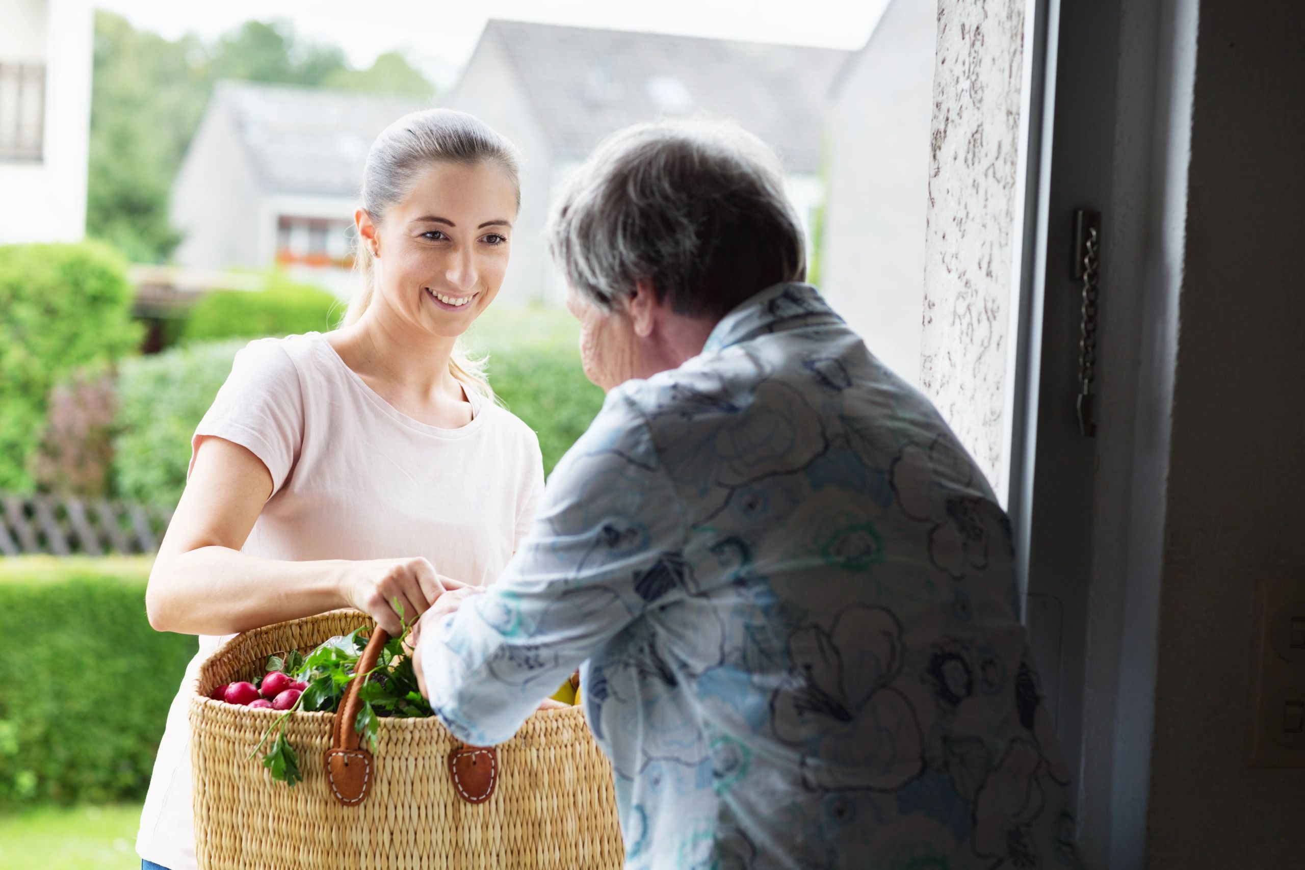 Caregiver delivering a bag of groceries to a senior at her front door